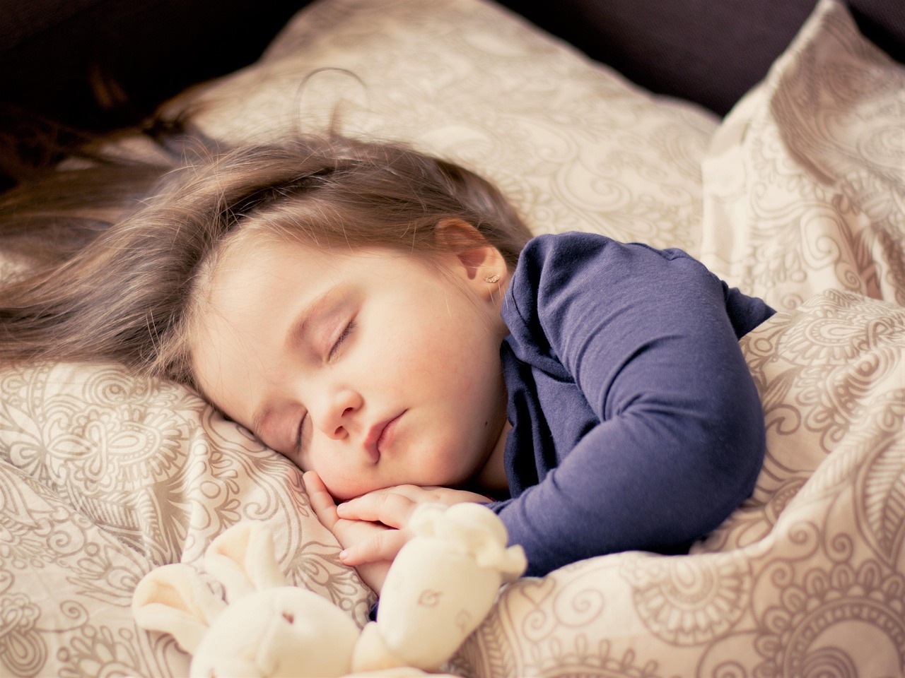 Jeune enfant endormi paisiblement dans son lit avec une peluche