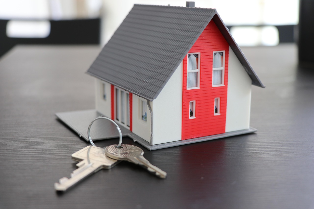 Petite maquette de maison rouge et blanche avec un trousseau de clés, fond noir