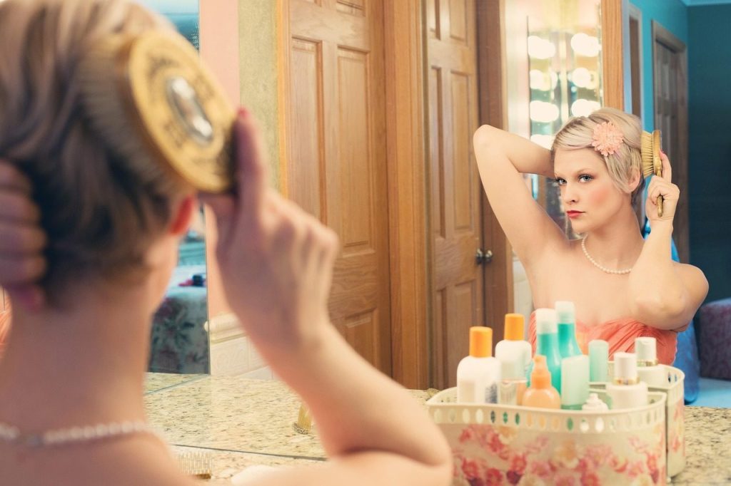 Jeune femme appliquant une crème de définition sur ses cheveux bouclés humides devant un miroir de salle de bain