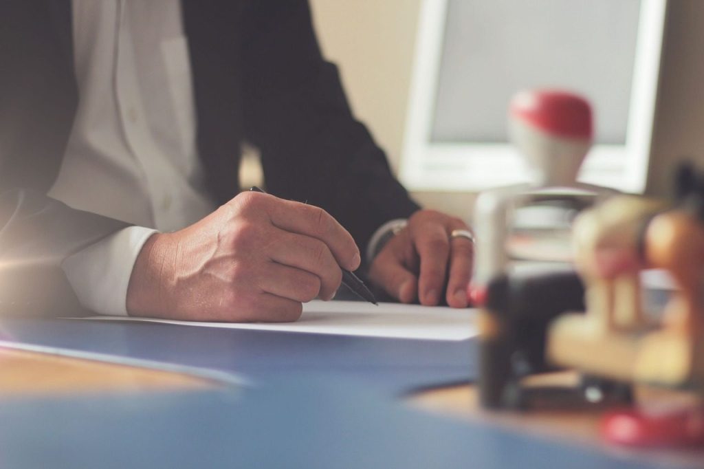 Main qui signe un document officiel, tampon rouge visible
