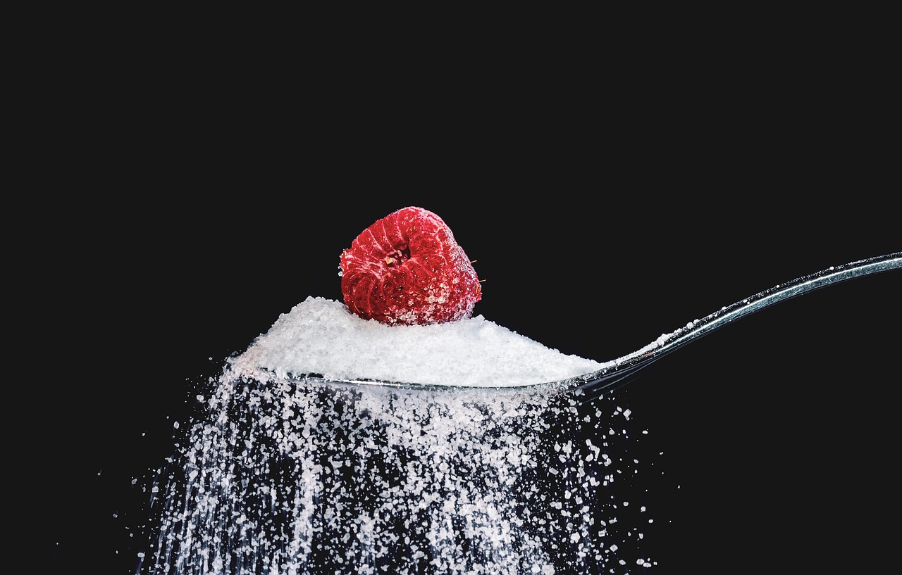 Cuillère de sucre en poudre avec une framboise, gros plan sur fond noir