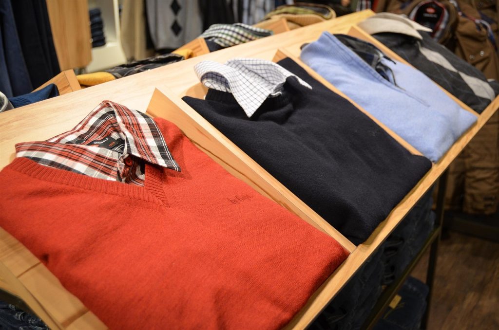 Chemises et pulls homme plies et ranges sur une etagere en bois de boutique